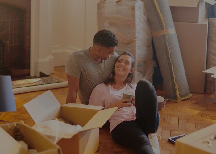 couple sat on floor smiling surrounded by moving home boxes
